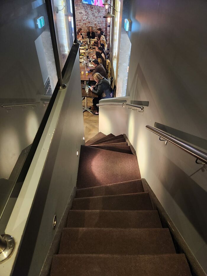 Narrow and steep death stairs leading down to a crowded dining area with people seated at a long table.