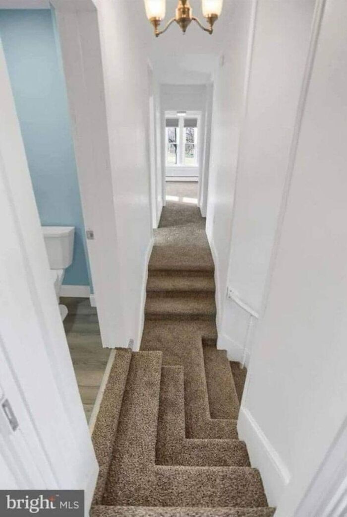 Narrow carpeted stairs with an unusual zigzag design in a bright white hallway, illustrating dangerous death stairs.