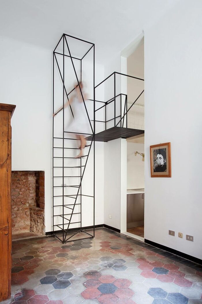 Minimalist death stairs made of thin black metal frame in a bright room with patterned tiled floor and blurred figure climbing.