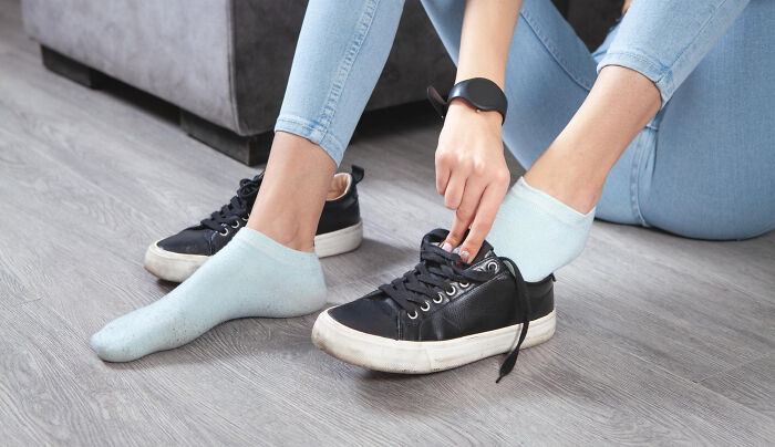 Person in light blue jeans sitting on the floor putting on black sneakers, illustrating comfort in a completely legal total psychopath context.