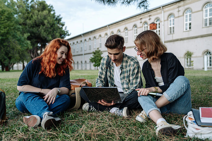 Three young adults sitting on grass outside, using a laptop, reflecting on parents wondering if they messed up their son