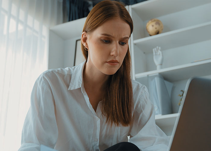 Young woman concentrating on laptop screen in a bright room, discovering creepy facts that captivate the brain.