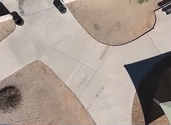 Aerial view of a park with walkways and patches of dirt and grass, showing tire marks from a pickup truck.