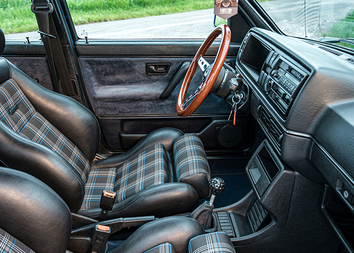 Interior of a vintage car with plaid seats and classic steering wheel showing still use daily obsolete design elements.