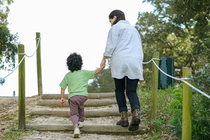 Woman holding child's hand walking up outdoor steps, illustrating colleague babysitting kids on day off concept Woman holding child's hand walking up outdoor steps, illustrating colleague babysitting kids on day off concept