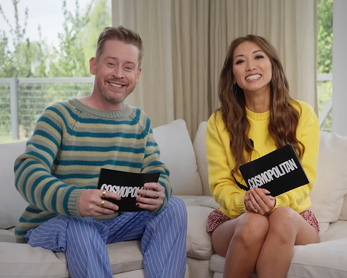 Two hosts sitting on a couch holding cards during an interview about a '90s child star's rare outing at age 44.