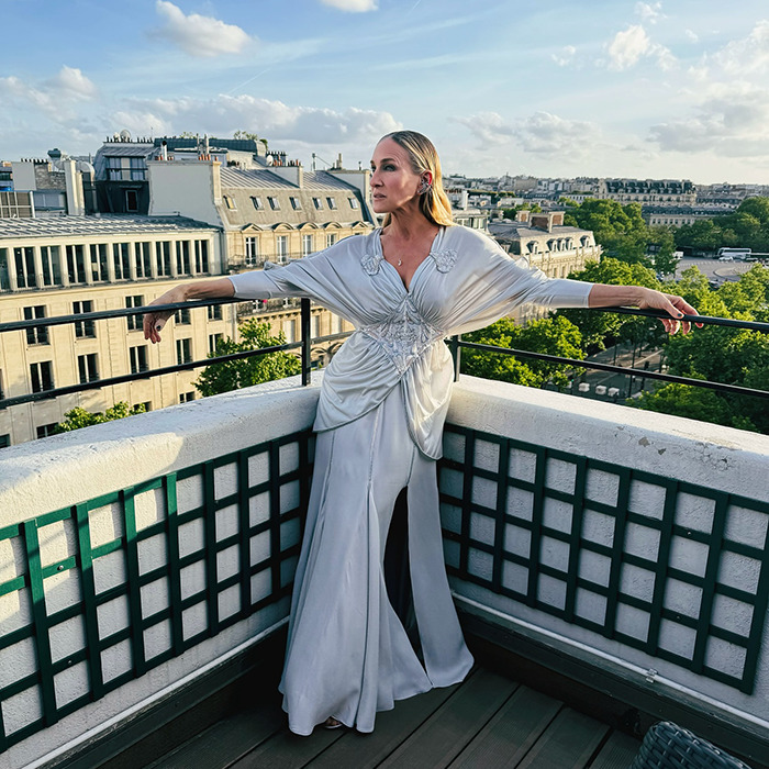 90s star in elegant white dress posing on a balcony with cityscape, revealing harsh comments from filming TV show.