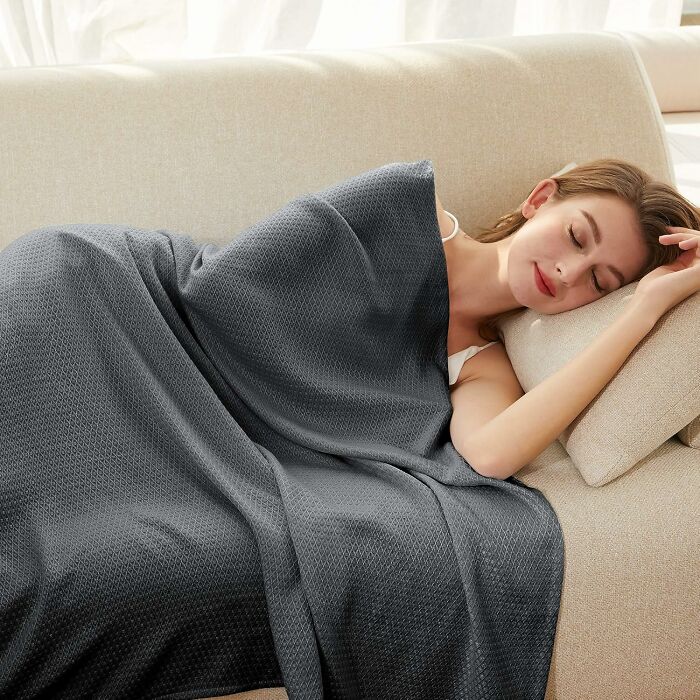 Woman resting on a beige couch covered with a gray blanket, illustrating ways to fight back summer annoyances naturally.
