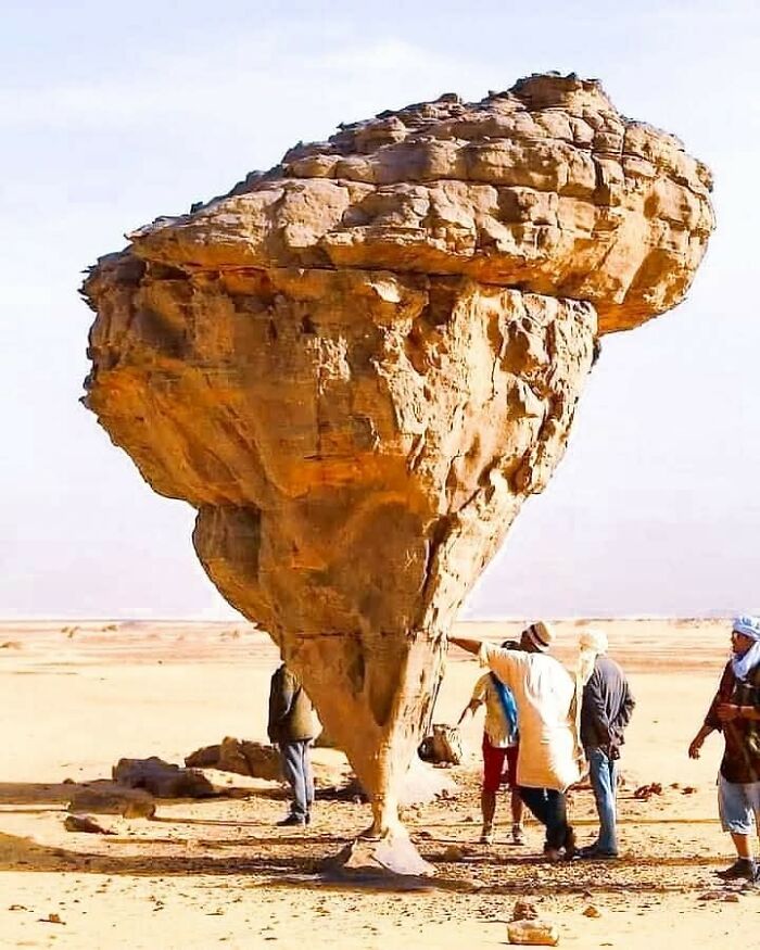 Unique balanced rock formation in a desert setting with people examining it, showcasing Archaeology World interest.