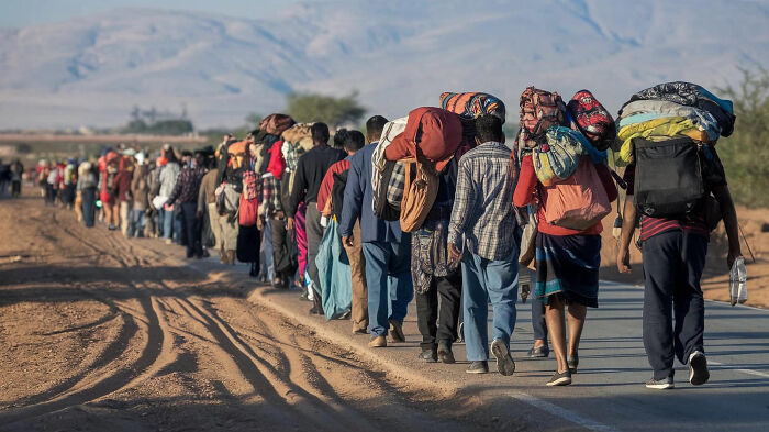 A long line of people carrying belongings on their backs walking along a dirt road, reflecting honest thoughts about the UK.