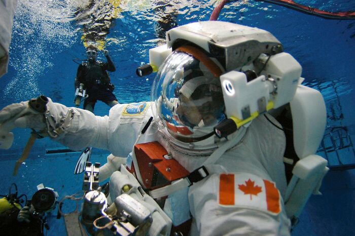 Astronaut in a training suit underwater with Canadian flag patch, preparing for space mission in a controlled environment.