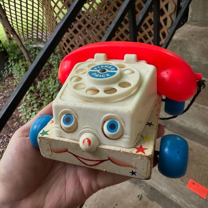 Vintage Fisher Price toy phone with red receiver and blue wheels held as a cool secondhand find outdoors near stairs.