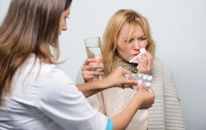 Woman with cold being offered medicine and water by a doctor, illustrating frustrating experiences with dismissive doctors.