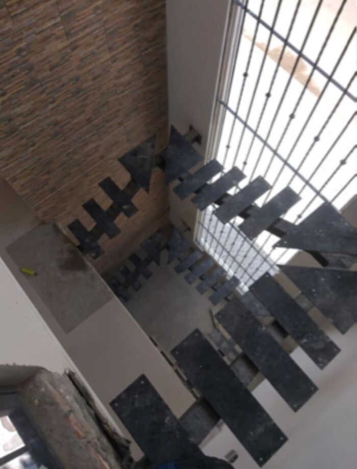 Spiral death stairs with missing steps and no railing inside a building near a large barred window.