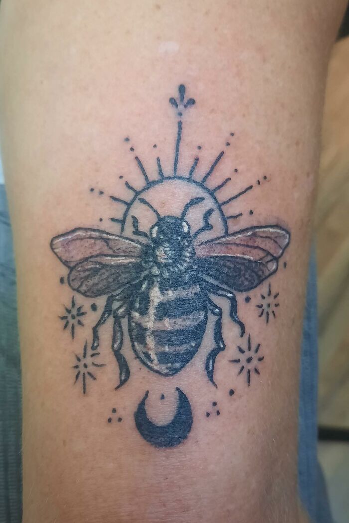 Tattoo of a bee with stylized sun rays and crescent moon on skin, an example of hilariously bad tattoos inkshaming.
