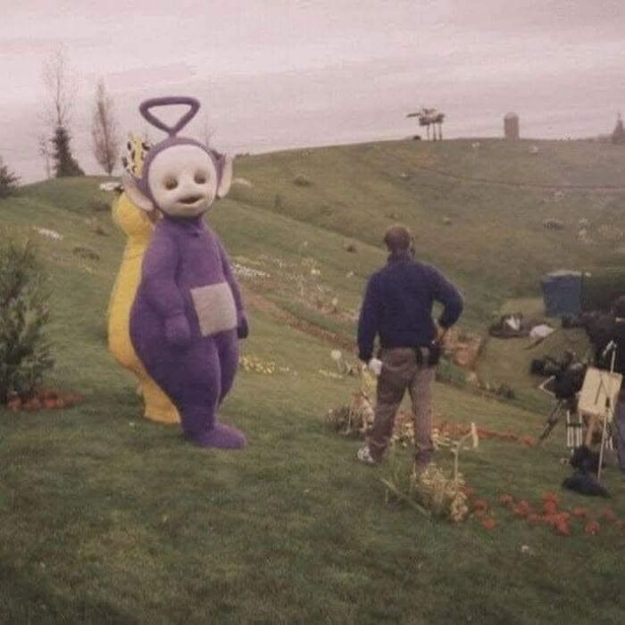 Behind the scenes of funny memes featuring a life-sized purple character on a grassy hill, adding humor to a hard day.