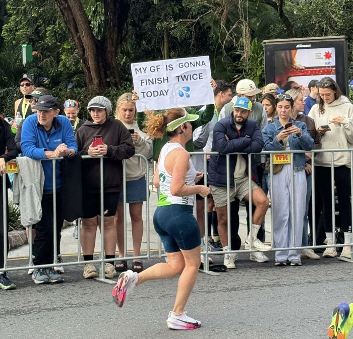 Crowd watching a marathon runner passing a humorous sign, funny posts with shareable content capturing real-life moments.