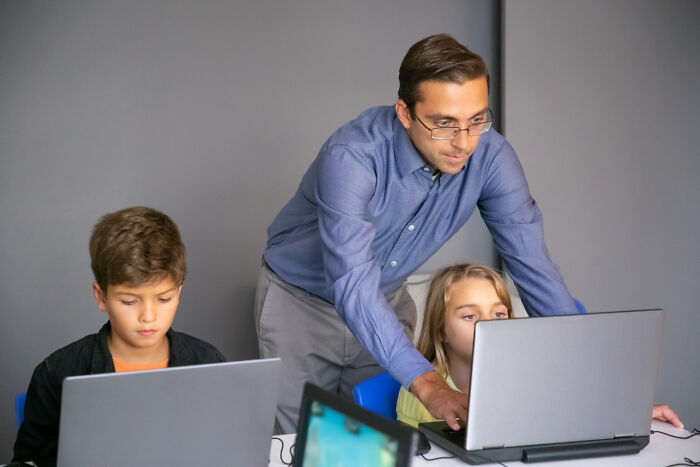 Man helping two children on laptops in a modern room, illustrating out-of-touch rich people flaunting their wealth online.