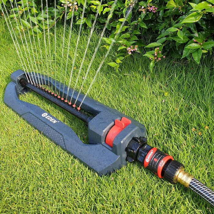 Oscillating garden sprinkler watering lush green grass as part of gardening tools and decor for an outdoor oasis.