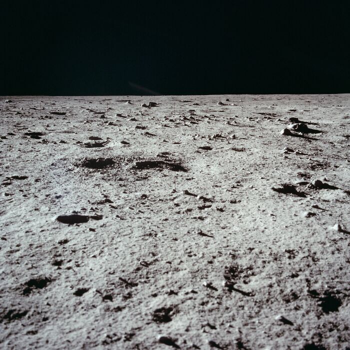Apollo mission photo showing the lunar surface with shadows and craters against the dark space background.