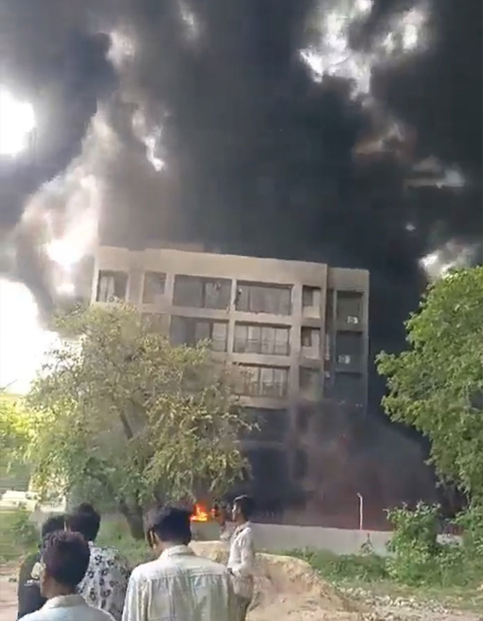 Thick black smoke billows from a building as people watch, linked to a horrifying plane crash and unusual take-off.