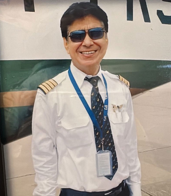 Survivor of Air India crash wearing pilot uniform and sunglasses, smiling in front of an aircraft on tarmac.
