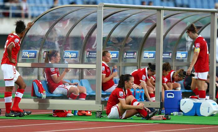 Female national soccer team players in red jerseys sitting and standing near the bench after a tough match against U15 boys team Female national soccer team players in red jerseys sitting and standing near the bench after a tough match against U15 boys team