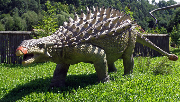 Life-like dinosaur model with spiked armor and long tail on green grass, illustrating dinosaur facts and prehistoric creatures.