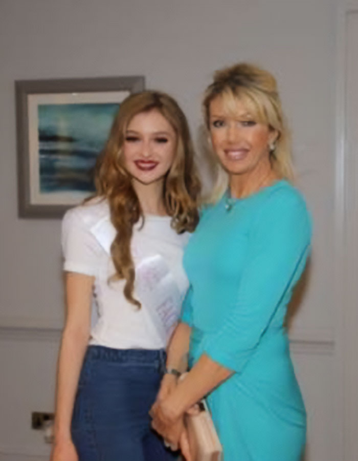 Anti-vax mom with her daughter, Cambridge 23YO graduate, standing together indoors smiling at the camera. Anti-vax mom with her daughter, Cambridge 23YO graduate, standing together indoors smiling at the camera.