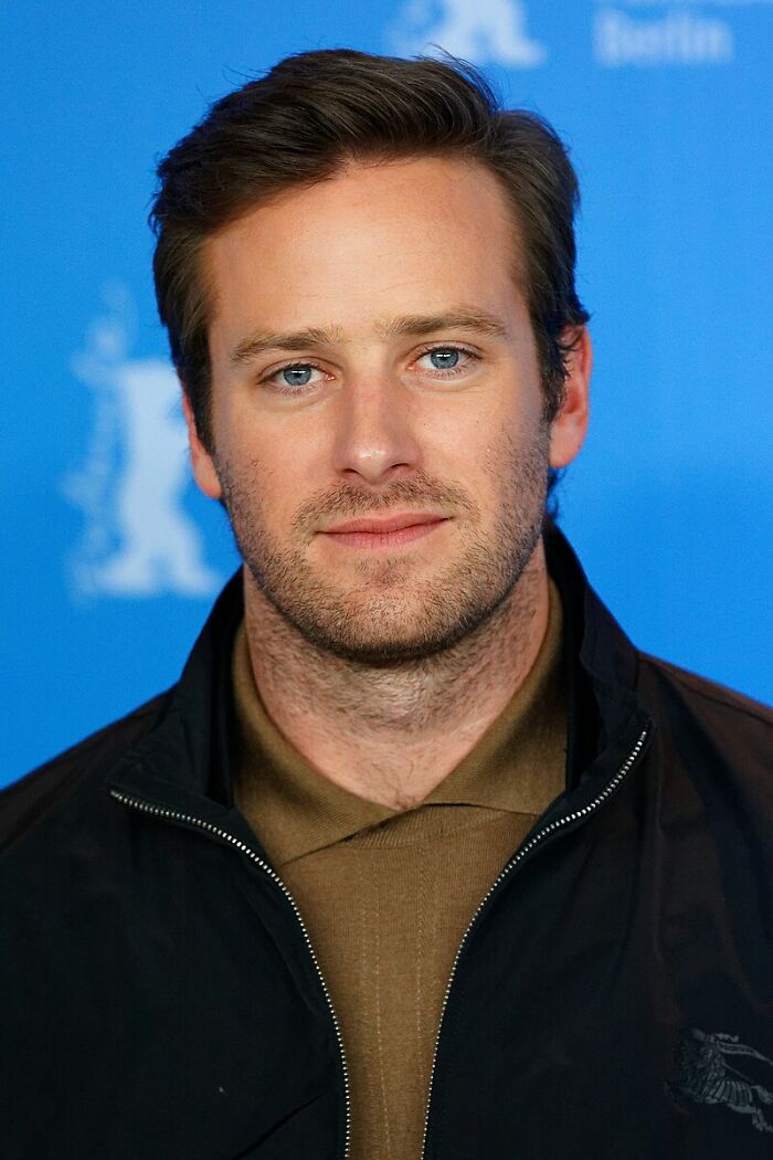 Close-up of a former Hollywood star with light beard and blue eyes posing against a blue background at an event.