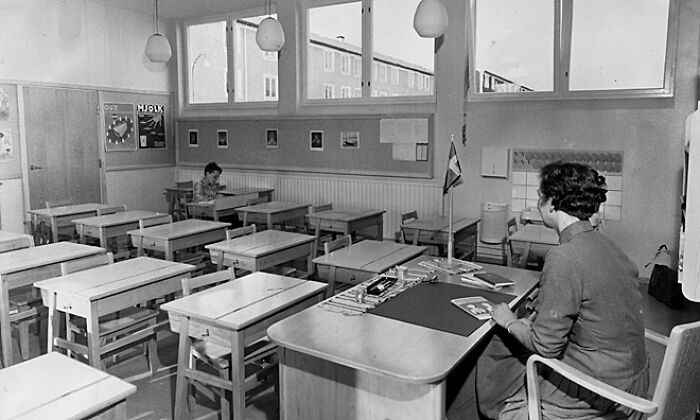Black and white photo of a classroom with a teacher and one student, representing historical events from the past.