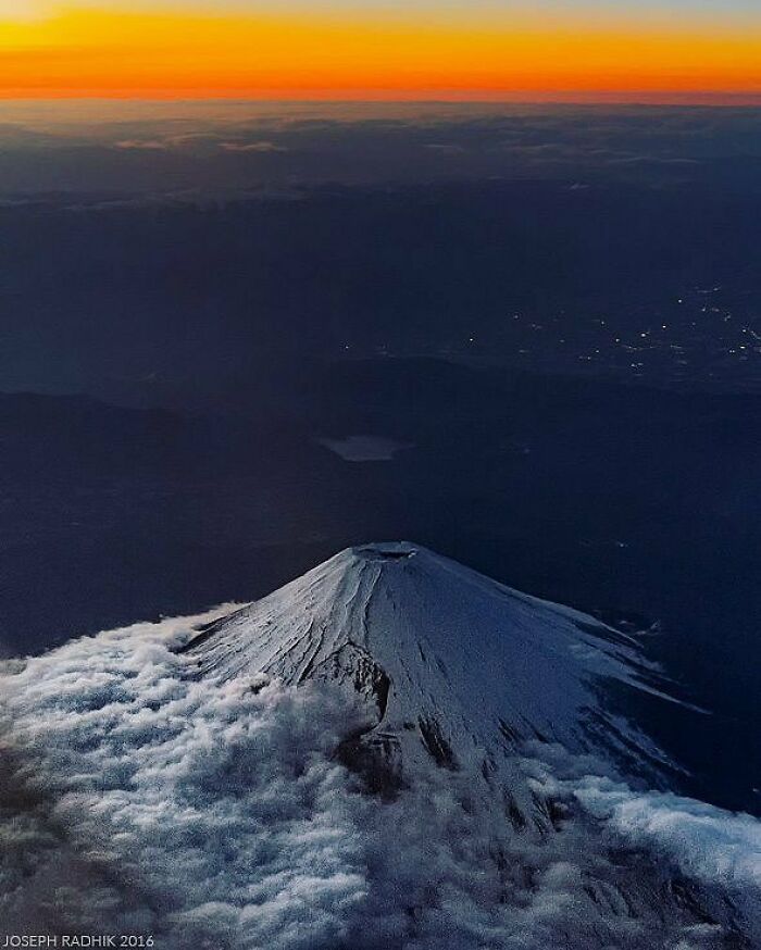 A famous landmark captured from an unexpected angle showing a snow-capped mountain peak rising above clouds at sunset.