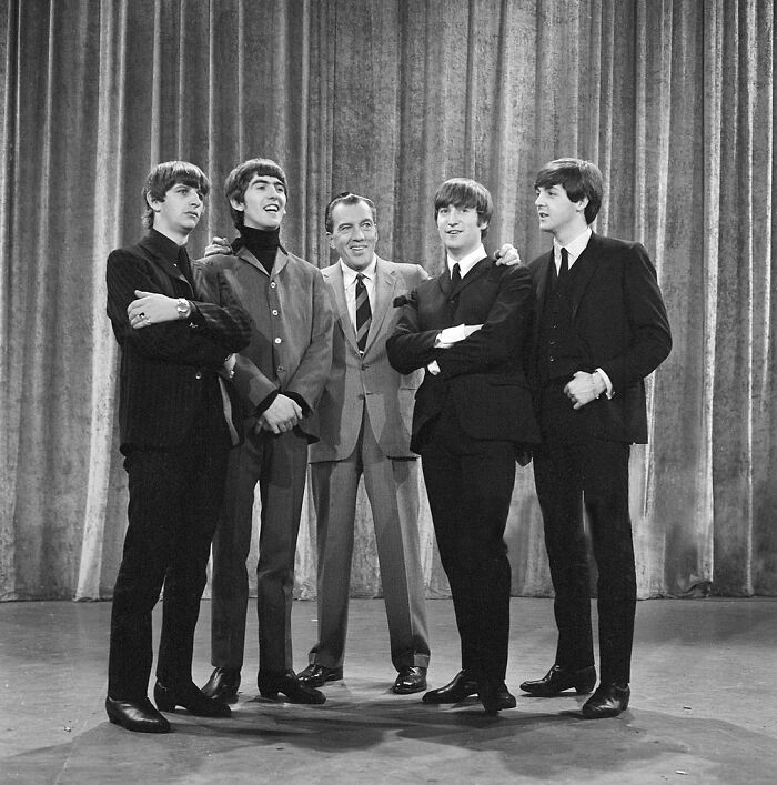 The Beatles with a host on stage, capturing a memorable I Was There When It Was Written moment in music history.