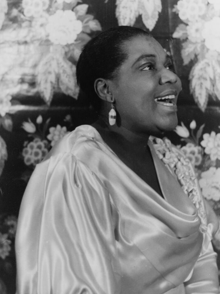 African American woman singing in elegant satin dress with floral background, capturing a Harlem Renaissance moment.