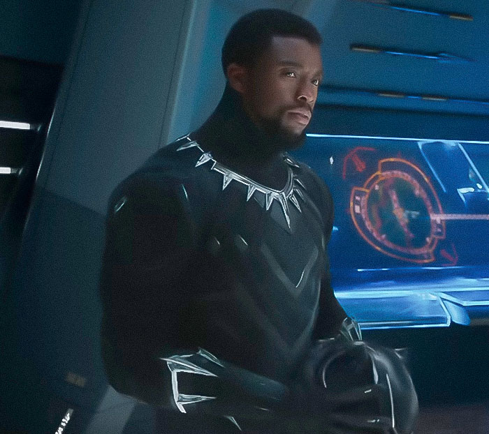 Black Panther character in a dark suit with silver necklace stands in a high-tech environment, sparking massive outrage online.