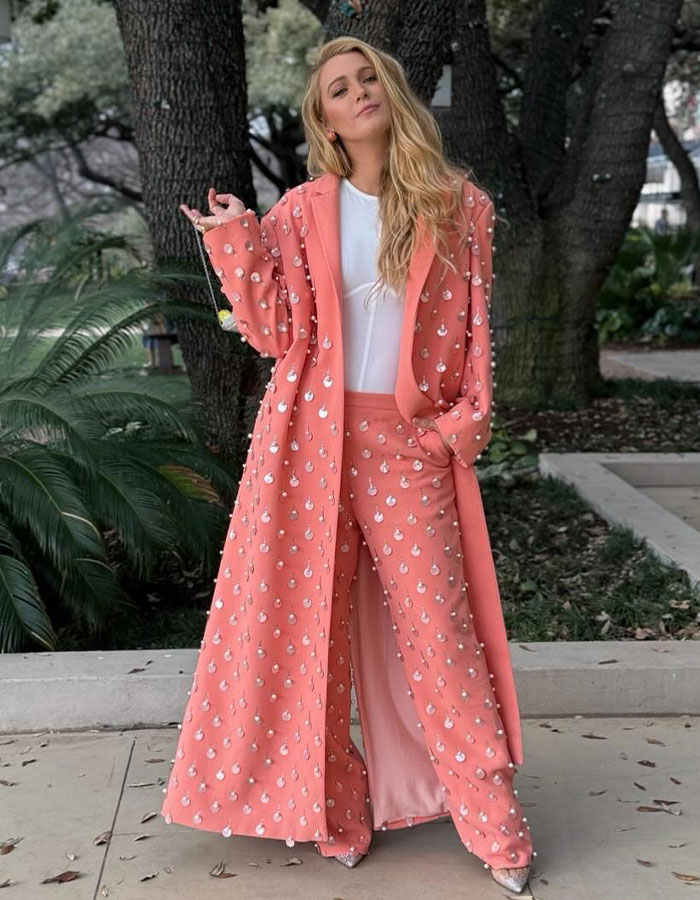 Blake Lively dressed in a pink embellished coat and pants, posing outdoors during a shopping trip amid backlash.