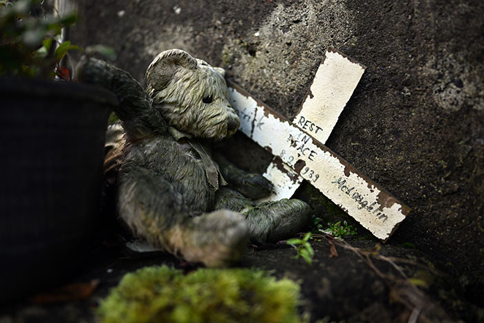Worn teddy bear next to a weathered cross memorial, symbolizing babies' bodies expected at Catholic home septic tank. Worn teddy bear next to a weathered cross memorial, symbolizing babies' bodies expected at Catholic home septic tank.