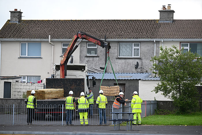 Workers in high-visibility gear operate a crane near houses at a site linked to septic tank investigation of babies' bodies. Workers in high-visibility gear operate a crane near houses at a site linked to septic tank investigation of babies' bodies.