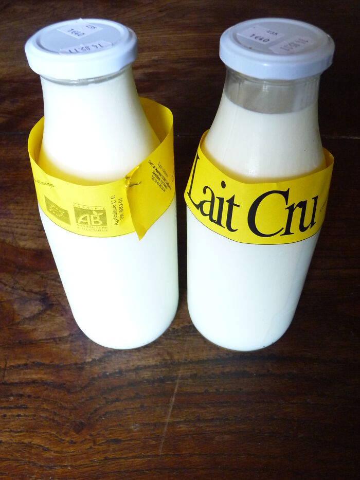 Two glass bottles of raw milk with yellow labels on a wooden surface, representing surprising foods banned in the USA.