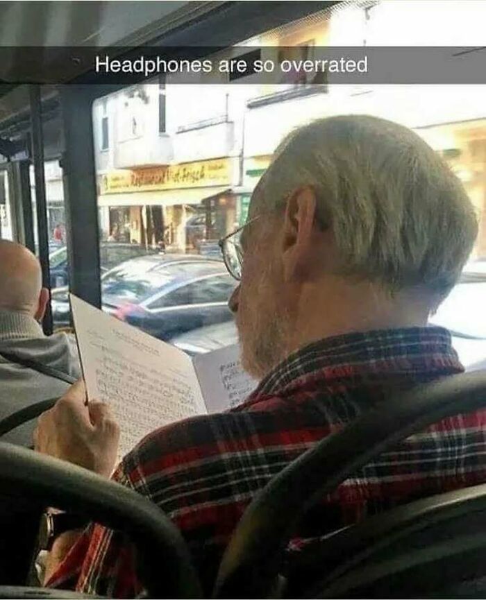 Older man reading sheet music on a bus with caption about headphones, intellectuals chuckling at memes humor.
