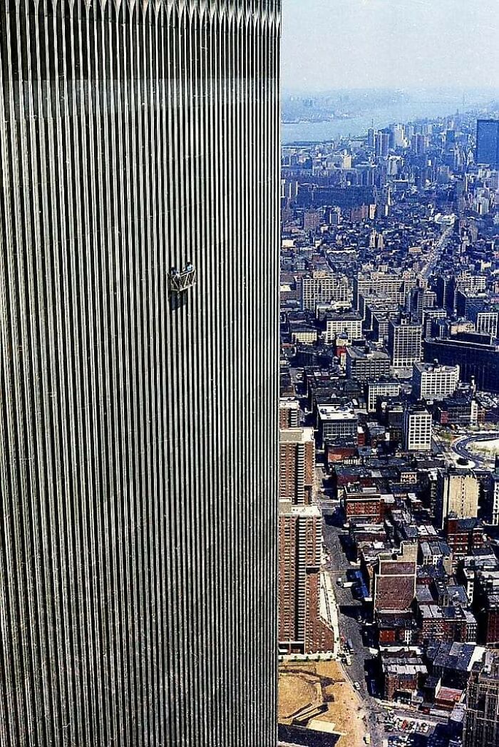 Historic photo showing window washers on a high-rise building overlooking a sprawling cityscape in a vintage urban scene.