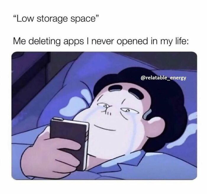 Person lying in bed with tears looking at phone, relatable energy meme about deleting unused apps for low storage space.