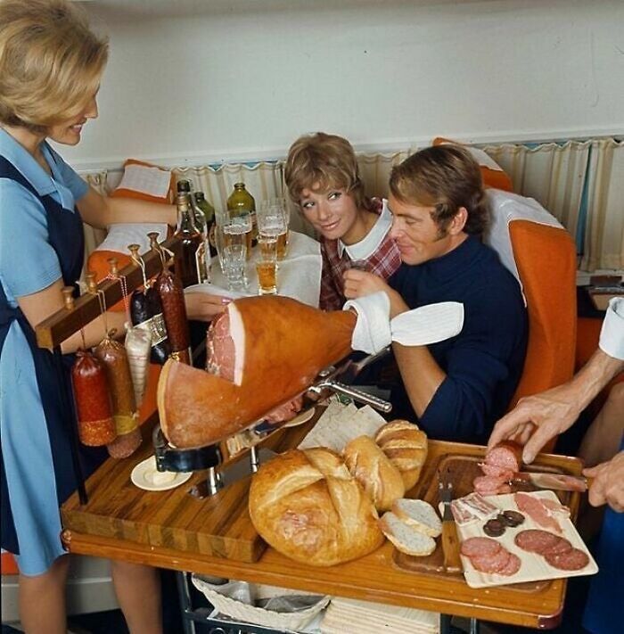Vintage scene of people enjoying sliced ham and sausages with bread and drinks, showcasing historic food traditions.