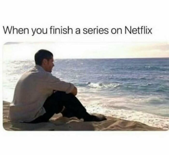 Man sitting alone on beach looking at ocean, capturing relatable energy of finishing a series on Netflix moment.