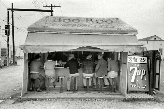Vintage roadside diner with six men seated on stools, showcasing history that looks confusing now in old black-and-white photo.