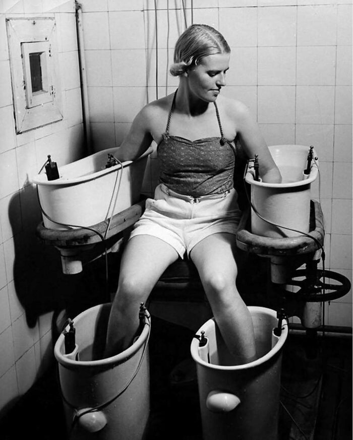 Woman with arms and legs submerged in vintage electrotherapy water baths, a confusing history pic showing old medical technology.