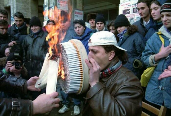 Man lighting a large circle of cigarettes on fire while a crowd watches in a historical confusing moment from history.