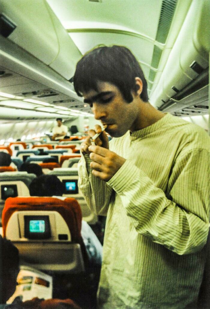 Young man smoking a cigarette inside an airplane cabin, a historical image showing past travel habits and behavior.