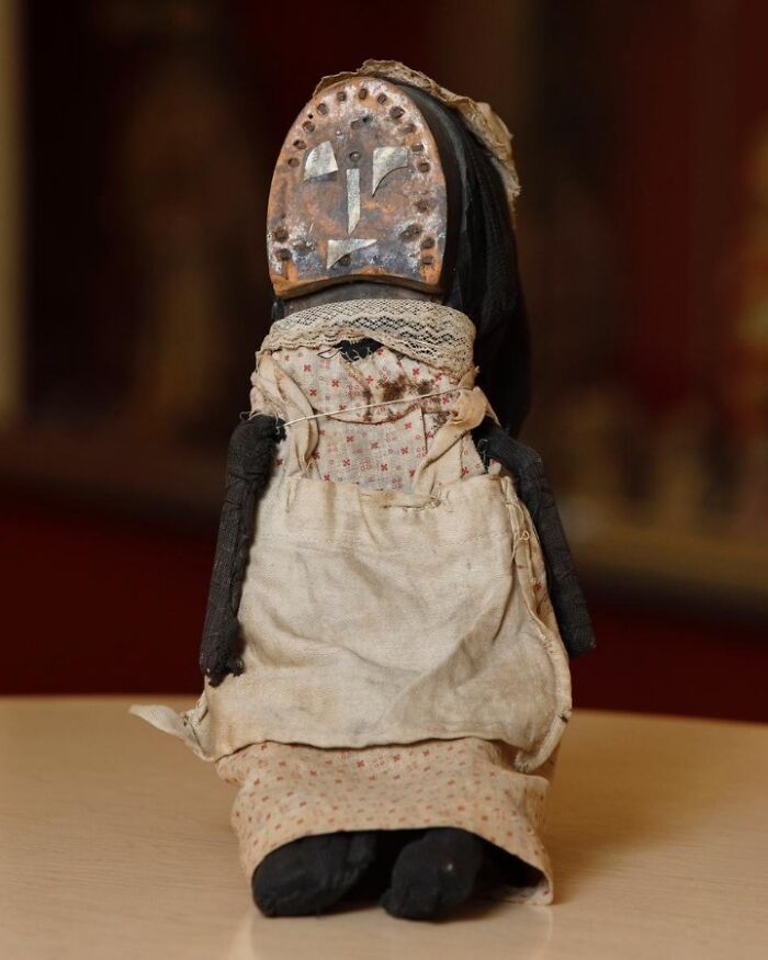 Old doll with a wooden mask face and worn fabric clothes, showcasing confusing historical design in vintage photos.