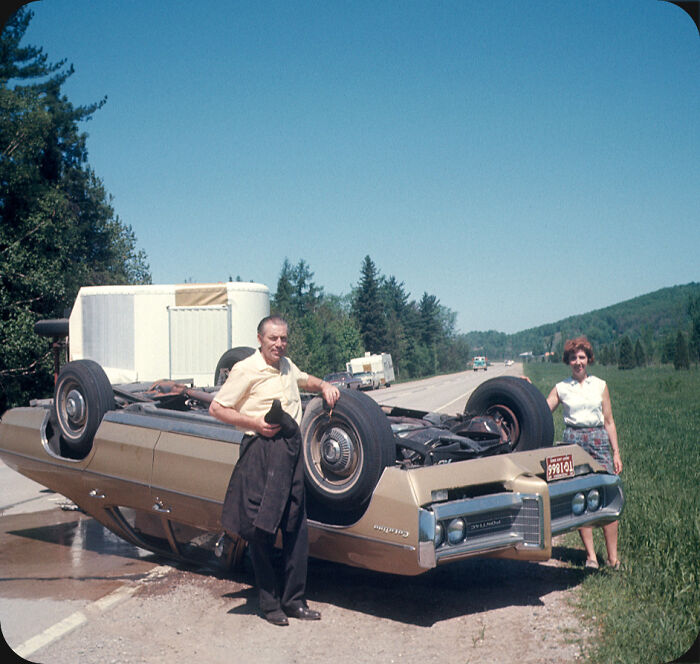 Man and woman standing beside an overturned vintage car on a roadside, a confusing look at history in a new pic.